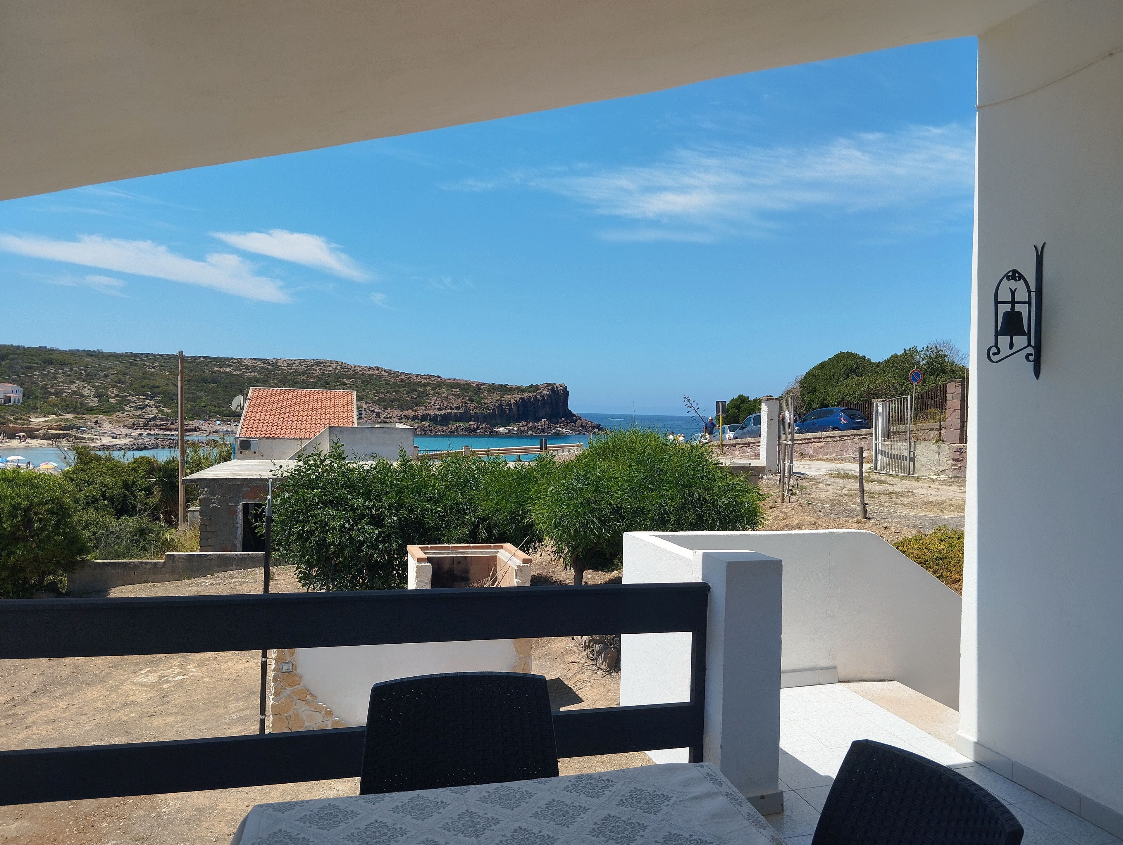 A balcony with a view of a beach, a building with a red roof, and a clear blue sky.