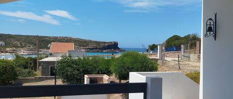 A balcony with a view of a beach, a building with a red roof, and a clear blue sky.