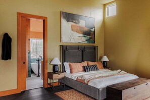 Une chambre à coucher avec un lit, des tables de chevet, une commode, un tableau et une vue sur la salle de bain.