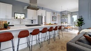 A modern kitchen with white cabinets, a stainless steel range hood, and a bar area with red stools.