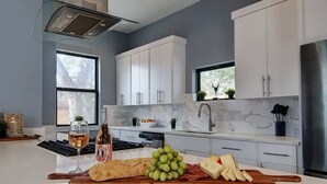A modern kitchen with white cabinets, a marble countertop, and a central island with food items and a wine glass.