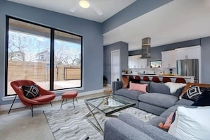 A modern living room with a gray sofa, red chair, and glass coffee table. - Deluxe Luxury Home | Hot Tub (Austin)