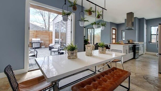 A modern kitchen with a white countertop, hanging plants, and a large window.