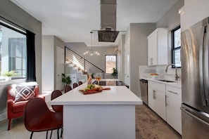 A modern kitchen with a central island, stainless steel appliances, and a staircase leading to an upper level. - Midcentury Luxury Home | Outdoor Deck (Austin)