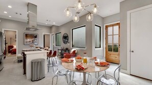 A modern kitchen with a central island, a dining area with a round table and chairs, and a large window providing natural light.