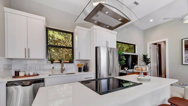 A modern kitchen with white cabinets, a stainless steel refrigerator, and a central island with a black induction cooktop.
