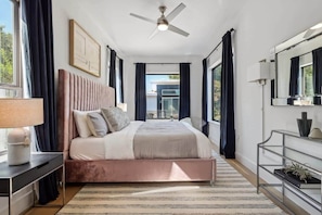 Quarto moderno com uma cama grande, um ventilador de teto, uma mesa de cabeceira e vista para o exterior.