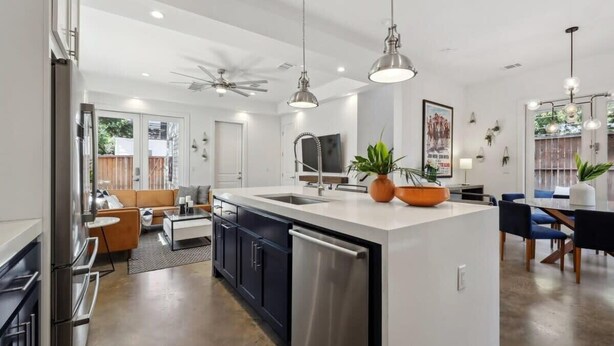 A modern kitchen with a central island, stainless steel appliances, pendant lighting, and a dining area with a table and chairs. - Luxe East Austin Home | Pool, Grill & Rooftop Deck (Austin)
