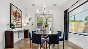 A dining area with a round table, six chairs, a chandelier, a poster on the wall, and a window with a view of the outdoors. - Luxe East Austin Home | Pool, Grill & Rooftop Deck (Austin)