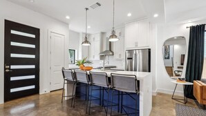 A modern kitchen with white cabinets, stainless steel appliances, and bar stools. - Luxe East Austin Home | Pool, Grill & Rooftop Deck (Austin)
