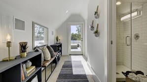 A modern, well-lit hallway with a bench, a rug, and a glass shower area. - Luxe East Austin Home | Pool, Grill & Rooftop Deck (Austin)