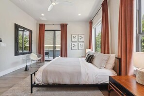 Une chambre à coucher moderne avec un grand lit, un bureau et une chaise. On y trouve des rideaux, un miroir et des tableaux encadrés au mur.