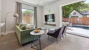 A modern living room with a green sofa, a glass coffee table, and a flat-screen TV mounted on the wall. - Luxe 5BR East Austin Home | Private Pool & Balcony (Austin)