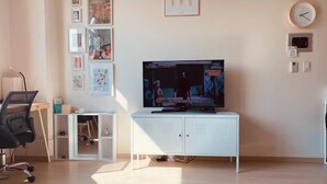 Un salon moderne doté d’un téléviseur à écran plat, d’un meuble blanc, d’un bureau avec une chaise et d’œuvres d’art accrochées au mur.