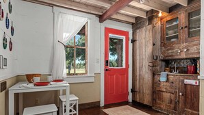 Une cuisine rustique avec une porte rouge, des armoires en bois et une table blanche avec des chaises.