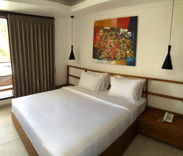 Habitación de hotel con una cama grande, dos mesitas de noche, un teléfono y un cuadro en la pared.