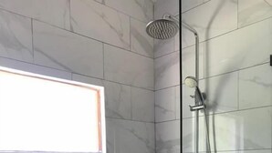 Una ducha moderna con puerta de vidrio, azulejos de mármol y un pequeño estante con artículos de aseo.