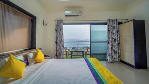 A hotel room with a bed, a wardrobe, a balcony with a table and chairs, and an air conditioning unit. - The Gren Villa Valley View (Mahabaleshwar)