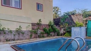 A swimming pool with metal ladders, surrounded by a stone wall and greenery. - The Gren Villa Valley View (Mahabaleshwar)