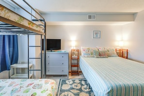 Une chambre avec un lit superposé, un bureau, une télévision et un lit recouvert d’une couverture à rayures.