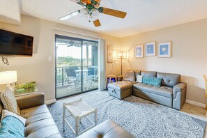 Un salon avec un ventilateur de plafond, un téléviseur, un canapé, une table basse et un tapis à motifs.