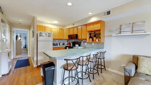 Una cocina moderna con armarios de madera, una isla central con taburetes y electrodomésticos como microondas y refrigerador.