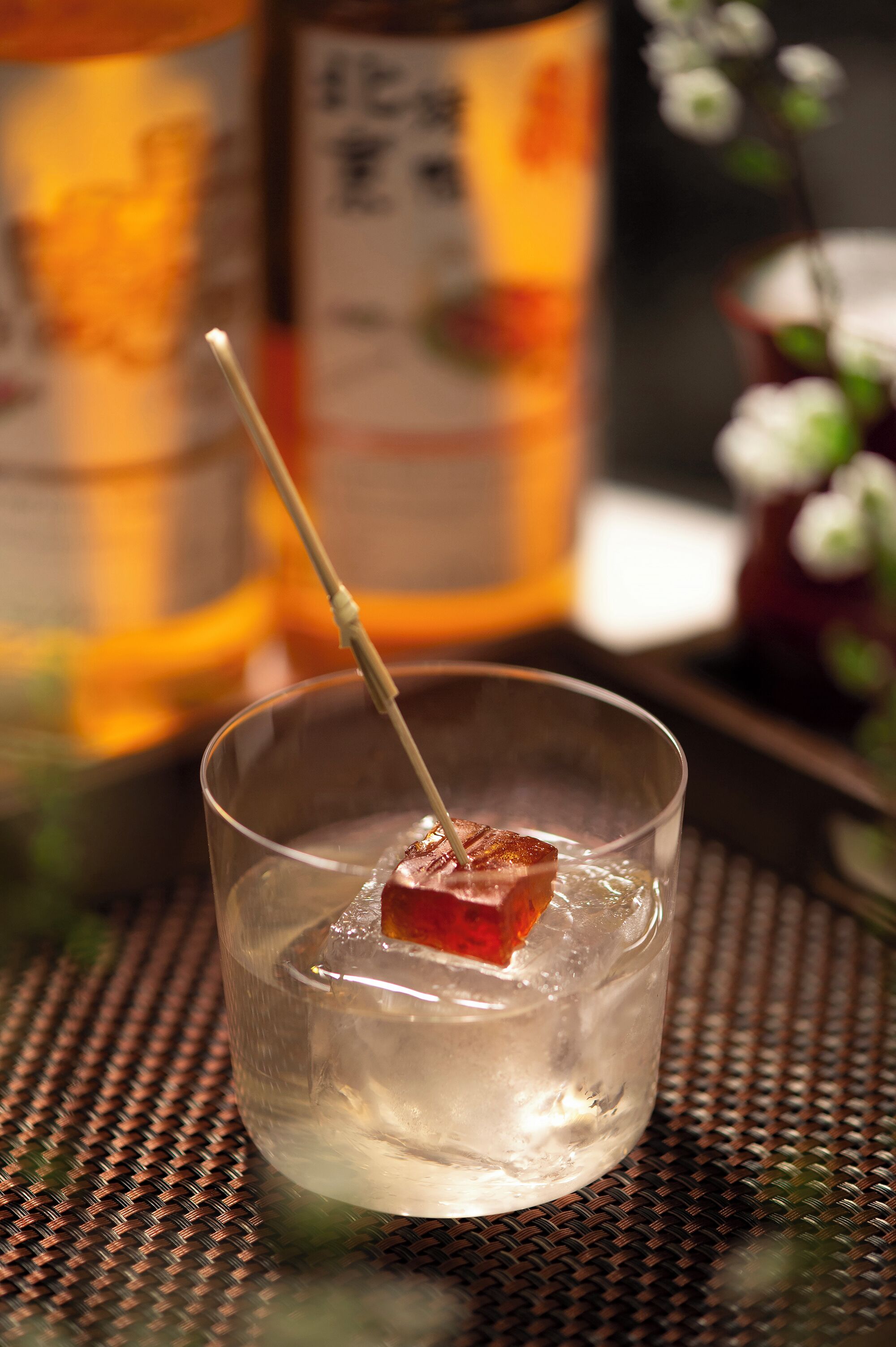 A glass with a cube of food on a woven surface.