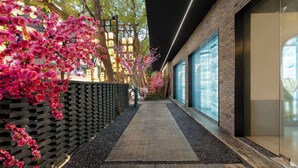 Un chemin bordé de fleurs roses et un mur de briques mènent à un bâtiment moderne doté de grandes fenêtres.