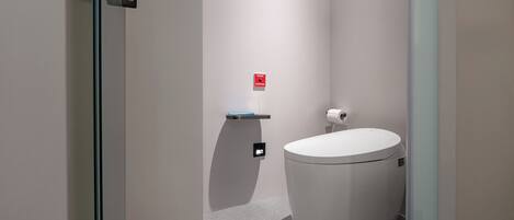 A modern bathroom with a toilet, a small shelf, and a red emergency button on the wall.