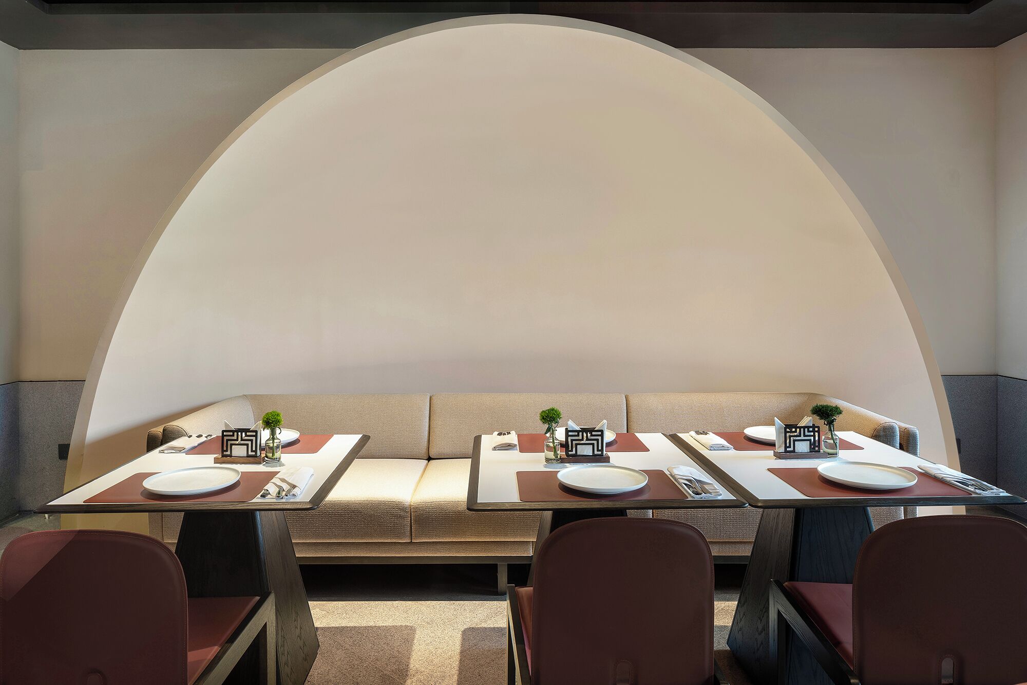 Een eetgedeelte met een lange tafel gedekt voor vier personen, zachte zittingen en een groot rondboogplafond.