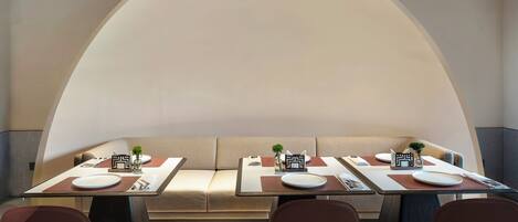 A dining area with a long table set for four, cushioned seating, and a large arched ceiling.