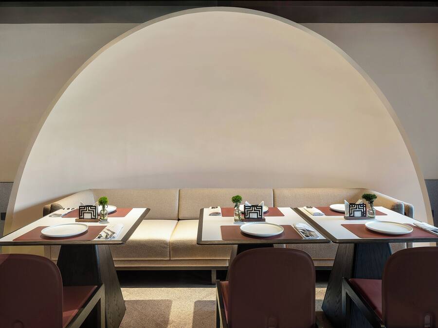A dining area with a long table set for four, cushioned seating, and a large arched ceiling.