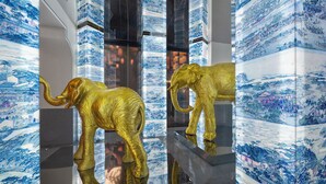 Un intérieur moderne avec des murs aux motifs traditionnels bleus et blancs, deux sculptures d’éléphants dorées et un sol réfléchissant.