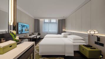 A modern hotel room with a large bed, a desk, a television, and a bedside table with a lamp.