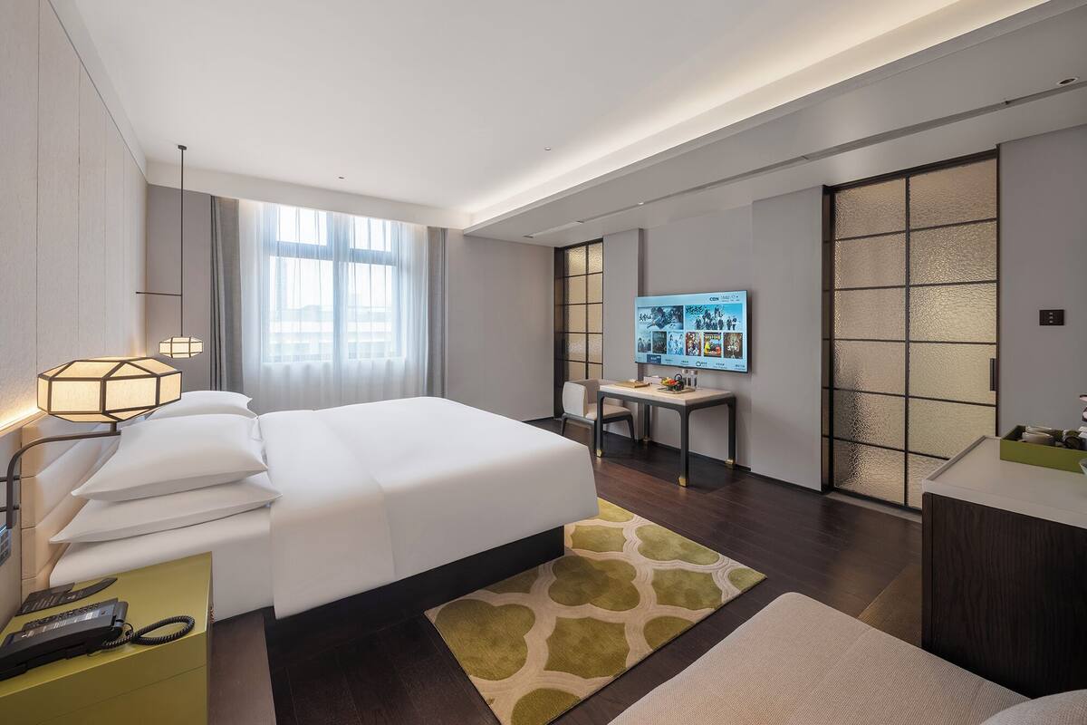 Una habitación de hotel moderna con una cama grande, un escritorio, un televisor y una puerta corredera.
