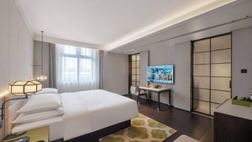 A modern hotel room with a large bed, a desk, a TV, and a sliding door.