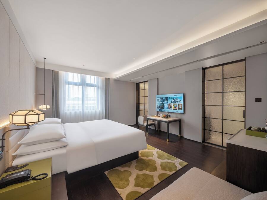 A modern hotel room with a large bed, a desk, a TV, and a sliding door.