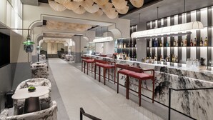 Un espace bar moderne avec des comptoirs en marbre, des tabourets de bar rouges et une variété de bouteilles d’alcool.