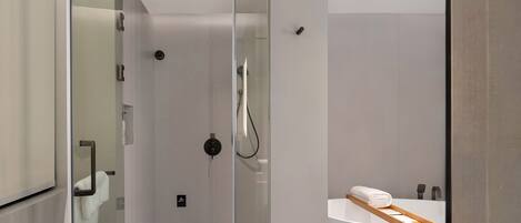Ein modernes Badezimmer mit einer gläsernen Duschkabine, einer weißen Badewanne mit Holztablett und einem minimalistischen Design.