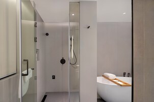Un baño moderno con ducha de vidrio, una bañera blanca con una bandeja de madera y un diseño minimalista.