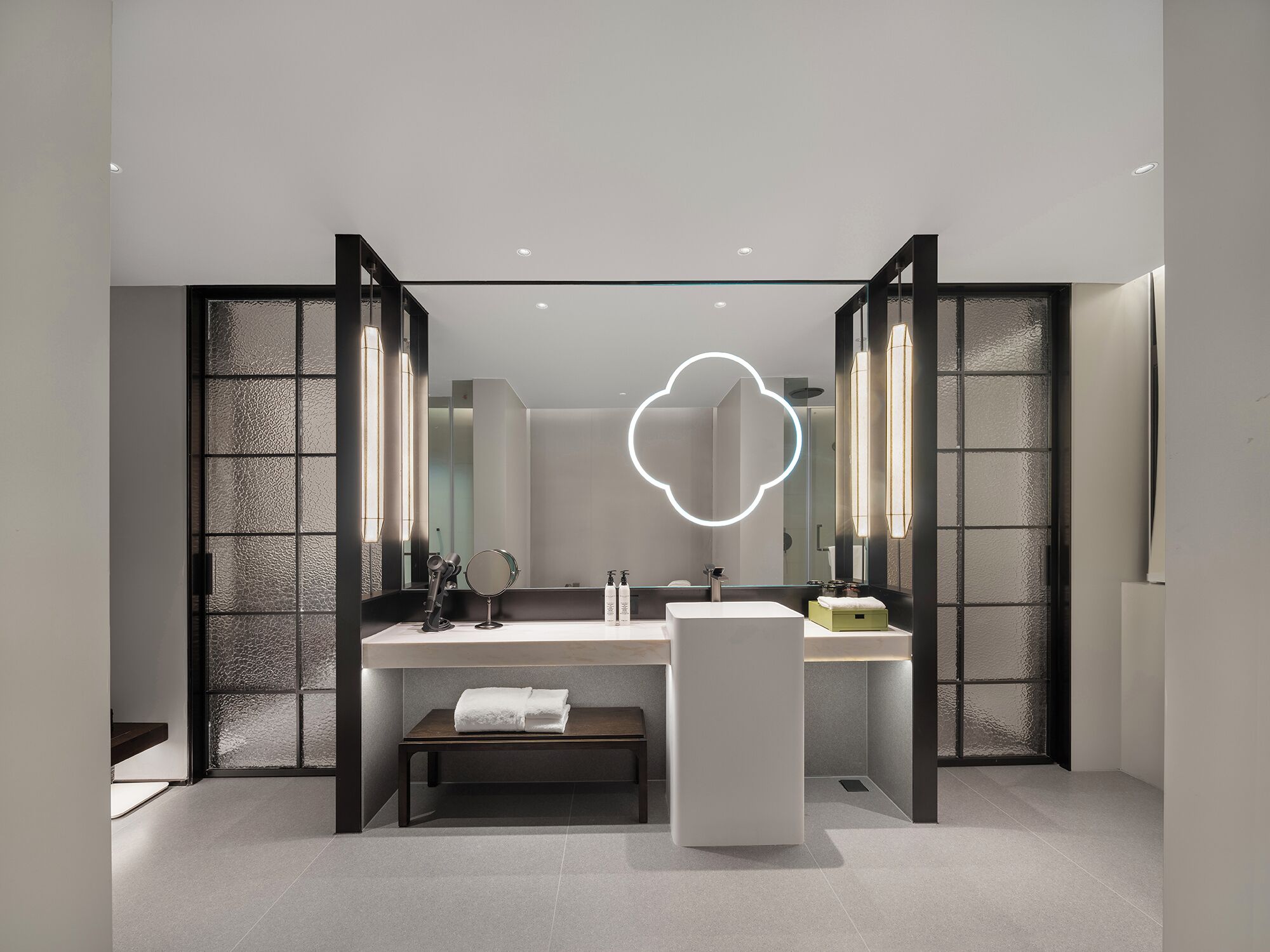 A modern bathroom with a large mirror, two sinks, and a bench.