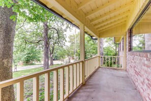 Eine überdachte Veranda mit Betonboden, Holzgeländer und Blick auf Bäume und eine Straße.