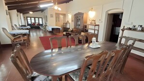 Un vaste espace dédié à la salle à manger, avec une grande table et des chaises en bois, un tapis rouge et, au fond, une cuisine moderne.