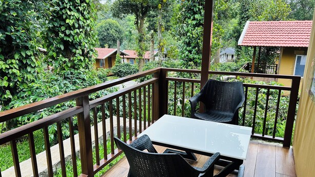 Un balcone con tavolo e sedie, immerso nel verde e con un edificio a tetto rosso sullo sfondo.