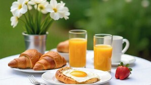 Una colazione con croissant, un uovo fritto, succo di frutta e una fragola su un tavolo bianco.
