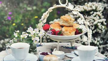 Ein gedeckter Tisch mit Teeservice, Scones, Erdbeeren und einer Blumenkomposition.