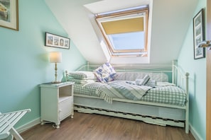 A bedroom with a sloped ceiling, a skylight, a bed with checkered bedding, a bedside table with a lamp, and a small white dresser.