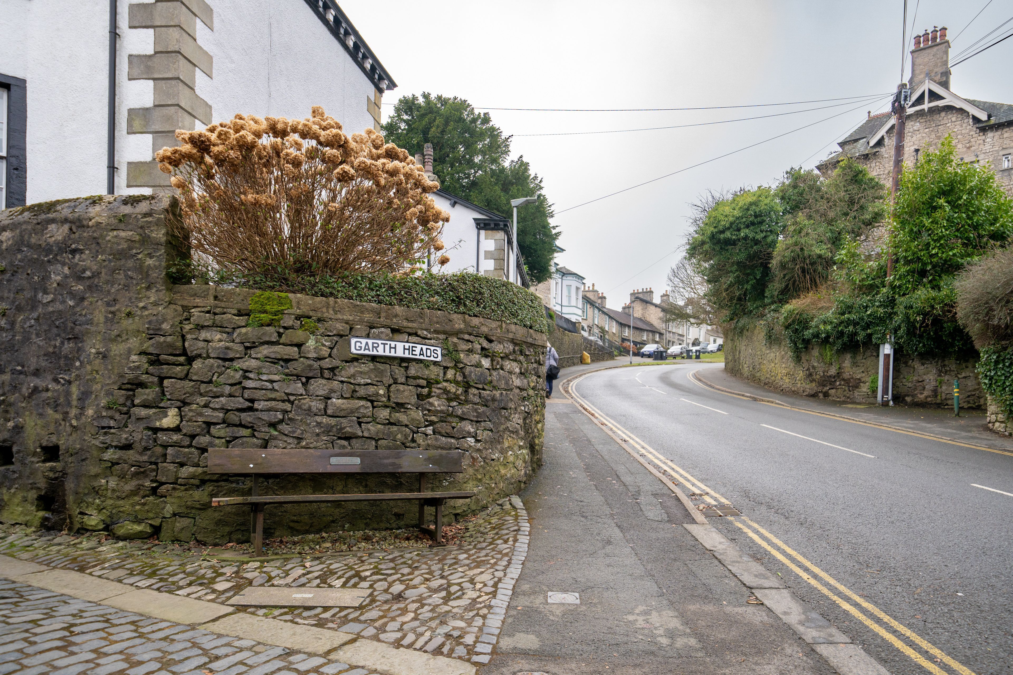 A stone wall with a bench and a sign reading "Garth Heads".