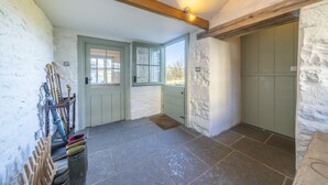Ein Raum mit Steinboden, einem Holzbalken an der Decke, einer grünen Tür und einem Fenster.