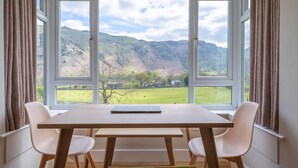 Un espace repas comprenant une table et des chaises, de grandes fenêtres offrant une vue sur une vallée verdoyante et des montagnes.